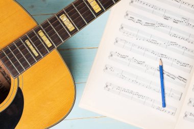 Gitar, nota kağıtları ve tahta masadaki kalemle müzik kaydı sahnesi, yakın plan.