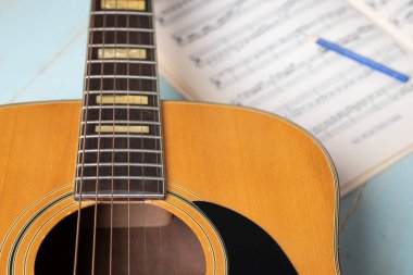 Gitar, nota kağıtları ve tahta masadaki kalemle müzik kaydı sahnesi, yakın plan.