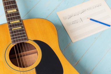 Gitar, nota kağıdı ve kalemle ahşap masada müzik kaydı sahnesi, yakın plan.