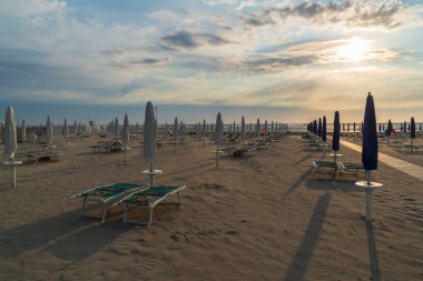 Kumsal ve güneş doğarken kapalı şemsiyeler, tipik İtalyan Adriyatik plajı. Lido Adriano, Emilia Romagna, İtalya..