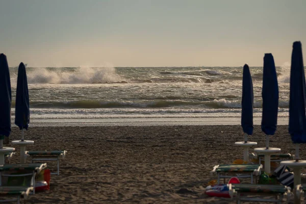 Big waves roll up on the beach. close parasol in bright Sunny day. White foaming waves and splashes.A hot summer day and high wave, seascape.Italy