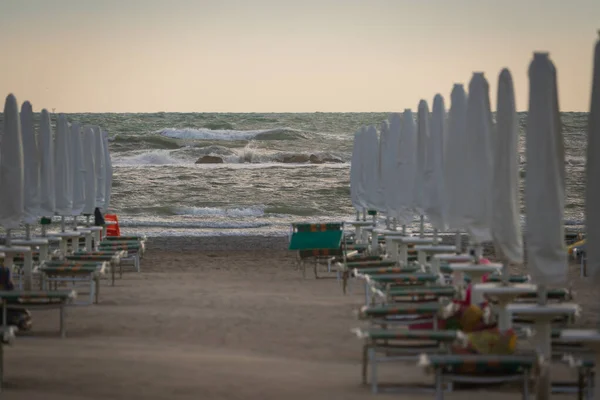 Big waves roll up on the beach. close parasol in bright Sunny day. White foaming waves and splashes.A hot summer day and high wave, seascape.Italy