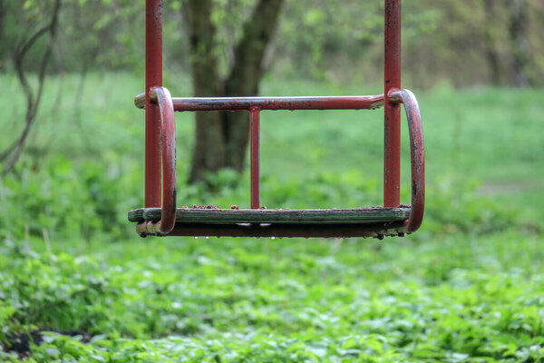 Детские металлические качели в парке на фоне травы