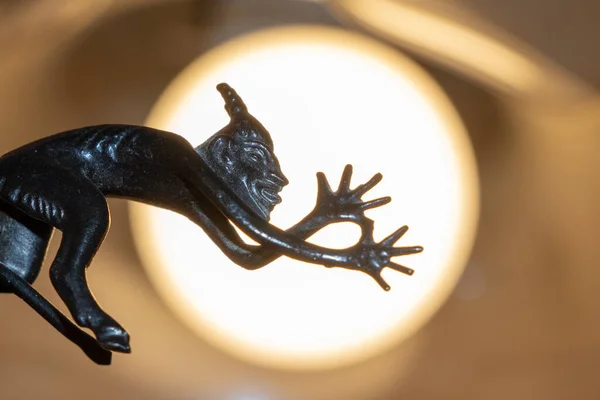 A small metal sculpture of the devil with a tail showing his tongue