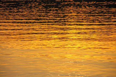 Gün batımı göletteki suda parlıyor.