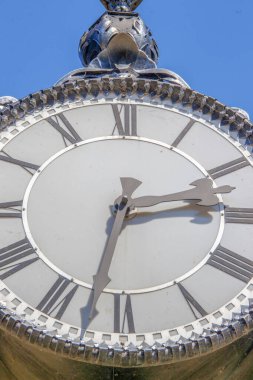 Parktaki bir sokak saatinin metal kadranı ve sandalyeleri