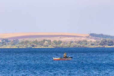Gölde bir teknede bir balıkçı balık yakalar.