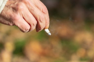 Sonbahar parkında elinde sigara tutan yaşlı bir adam.
