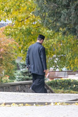 Siyah cüppeli bir rahip parktan kiliseye doğru yürür.
