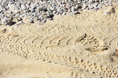 Sarı kumda araba lastiği izleri var.