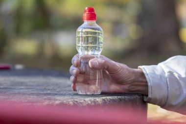 Yaşlı bir adam elinde bir şişe su tutuyor.