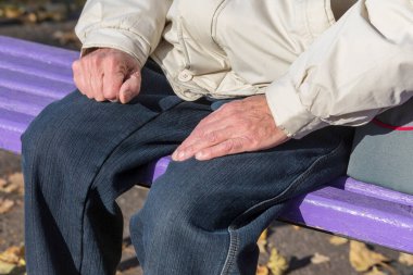 Yaşlı bir adam parkta bir bankta oturur ve güneşin tadını çıkarır.