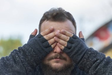 Sakallı ve bıyıklı bir adam elleriyle gözlerini kapatır.