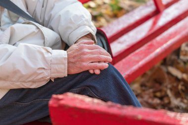 Parkta dizlerinin üstünde yaşlı bir adamın elleri.