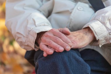 Parkta dizlerinin üstünde yaşlı bir adamın elleri.