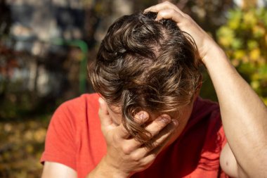 Kırmızı tişörtlü bir adam umutsuzluk içinde ve elleriyle başını örttü.