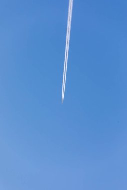 Uçak mavi gökyüzünde uzanıyor ve beyaz bir iz bırakıyor.