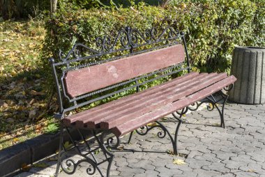 Ağaçların yanındaki parkta kırmızı ahşap bir bank.