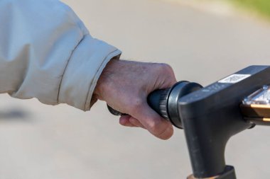 Parkta scooter 'ın sapını tutan yaşlı adam.
