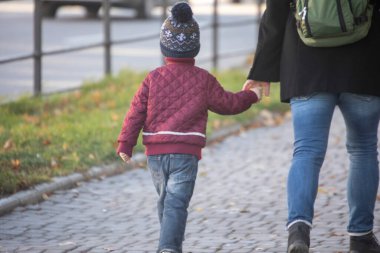 Annesiyle sokakta yürüyen bir çocuk.