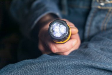 Bir adam elinde bir cep feneri tutar.