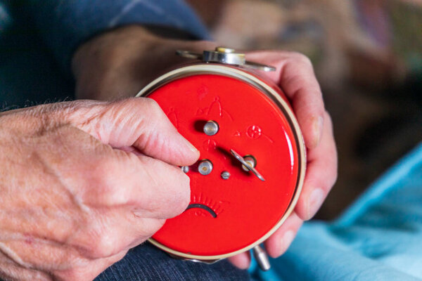 Старик держит красные механические часы