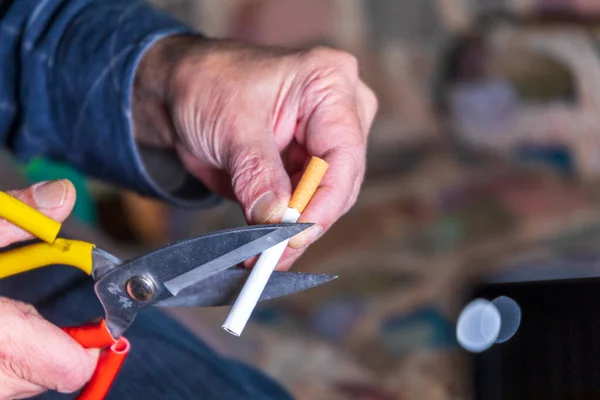 A man holds scissors and a cigarette in his hand, he tries to cut it to quit smoking