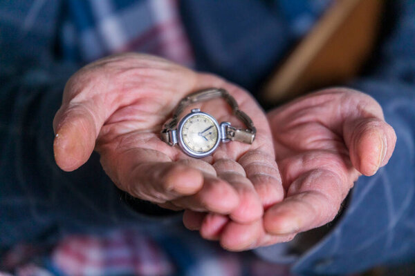 Старик держит в руках женские часы своей жены.