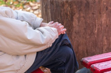 Parkta dizlerinin üstünde yaşlı bir adamın elleri.