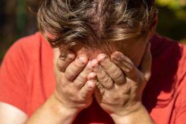 Kırmızı tişörtlü bir adam umutsuzluk içinde ve elleriyle başını örttü.