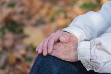 Parkta dizlerinin üstünde yaşlı bir adamın elleri.