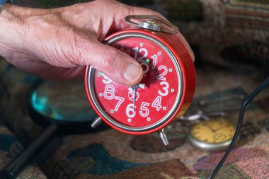 Yaşlı adam kırmızı mekanik bir saat tutuyor.