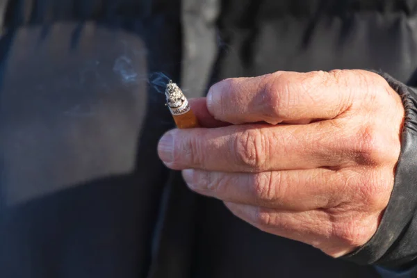 Old man smokes a cigarette on the street. Cigarette in hand