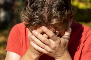 Kırmızı tişörtlü bir adam umutsuzluk içinde ve elleriyle başını örttü.