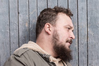 Ahşap bir duvarda sakallı genç bir adamın profili.