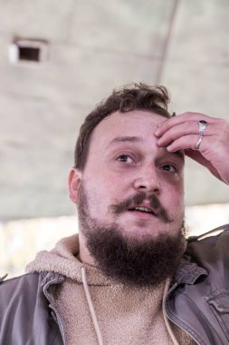 Sakallı ve bıyıklı genç bir adamın kafası karışıktır ve kendini güvensiz hisseder. Adam bir şeyler düşünmüş.