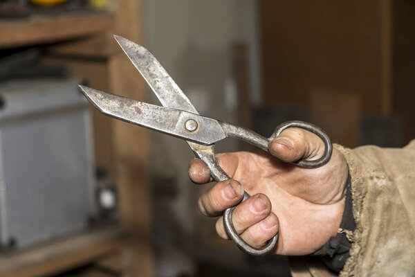 Мужчина держит в руке металлические ножницы в мастере