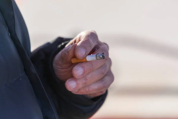 Old man smokes a cigarette on the street. Cigarette in hand