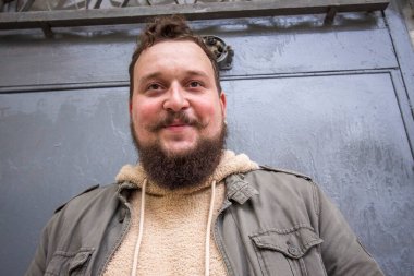 Sakallı genç bir adam gülümsüyor.