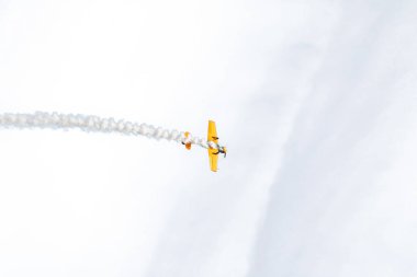 Beyaz arka planda bir uçak. Sarı bir uçak gökyüzünde uçuyor, ardında dumandan bir iz bırakıyor.