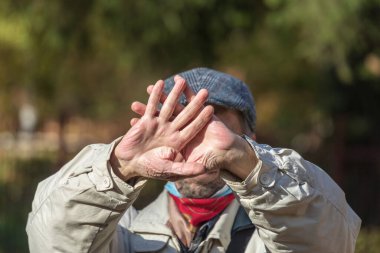 Yaşlı adam elleriyle yüzünü kapatıyor ve darbelerden ve tehlikeden sakınıyor.