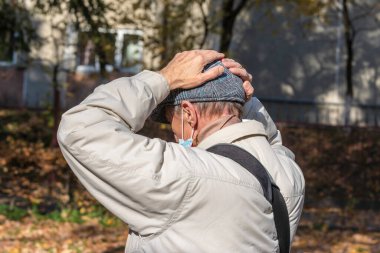 Yaşlı adam ellerini başının arkasında tutuyor ve umutsuzluk ve üzüntü içinde.