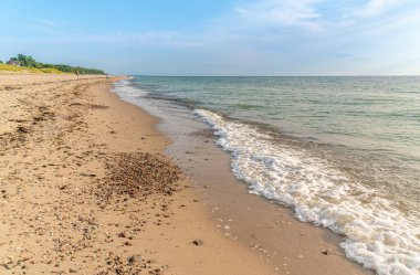 Kumsal kıyısı. Dalgalar çekildi. Kumlu bir sahilde dalgalar kırılıyor. Deniz kıyısı boyunca. Akşam havuzun üstüne düşüyor. Gün batımında deniz manzarası. Baltık Denizi kıyısında Tatil.