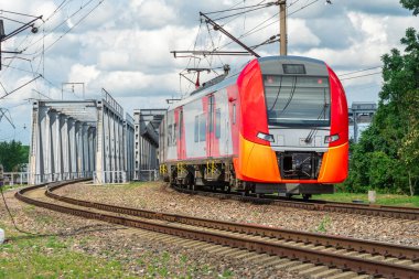 Bir elektrikli tren demir bir köprüyü geçer. Trenin rayların üzerindeki hareketi. Şehir ortamında banliyö treni.