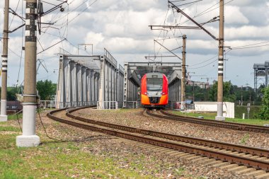Bir elektrikli tren demir bir köprüyü geçer. Trenin rayların üzerindeki hareketi. Şehir ortamında banliyö treni.