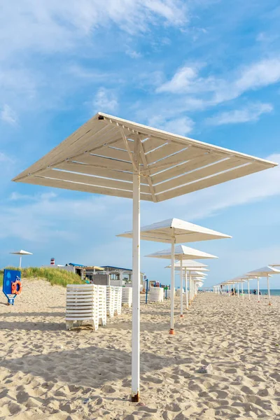 Deniz kıyısında güneşten ahşap şemsiyeler. Plaj sezonu kapanıyor. Plajda tatilciler için beyaz tasarımlar. Kumlu sahilde tatilciler için güneşten korunacak barınaklar var..