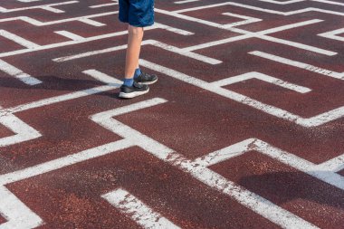 Asfalta çizilmiş bir labirent. Labirentten çıkmanın bir yolunu bul. Kırmızı yüzeyinde beyaz boya olan geometrik çizim. Çocukların mantıklı eğlencesi. Labirentte yürü.