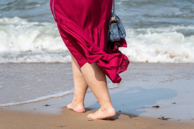 Deniz kıyısında kumda yürüyen bir kadının bacaklarının yakın çekimi. Kumlu sahil boyunca bir yürüyüş. Denizde yaz tatili. Plajda bir tatilci. Deniz suyunda bir yürüyüş.