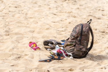 Plajda gezgin kıyafetleri. Ayakkabılar ve sırt çantası kumda yatıyor. Kumsalda dinleniyorum. Kumlu deniz kıyısında terk edilmiş giysiler. Turistler eşyalarını kıyıya bıraktılar..