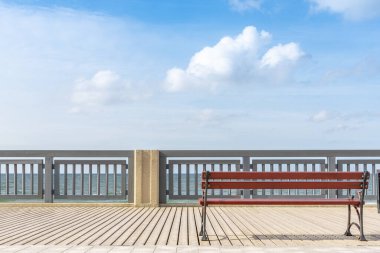 Deniz kenarında bir bank var. Tahta kaldırımda boş basit bir bank. Turistlerin dinlenip yürüyebileceği bir yer. Rıhtım boyunca raylar.